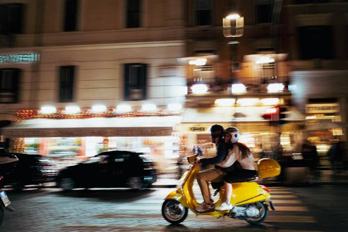 Photograph of a couple on a yellow scooter driving on a street